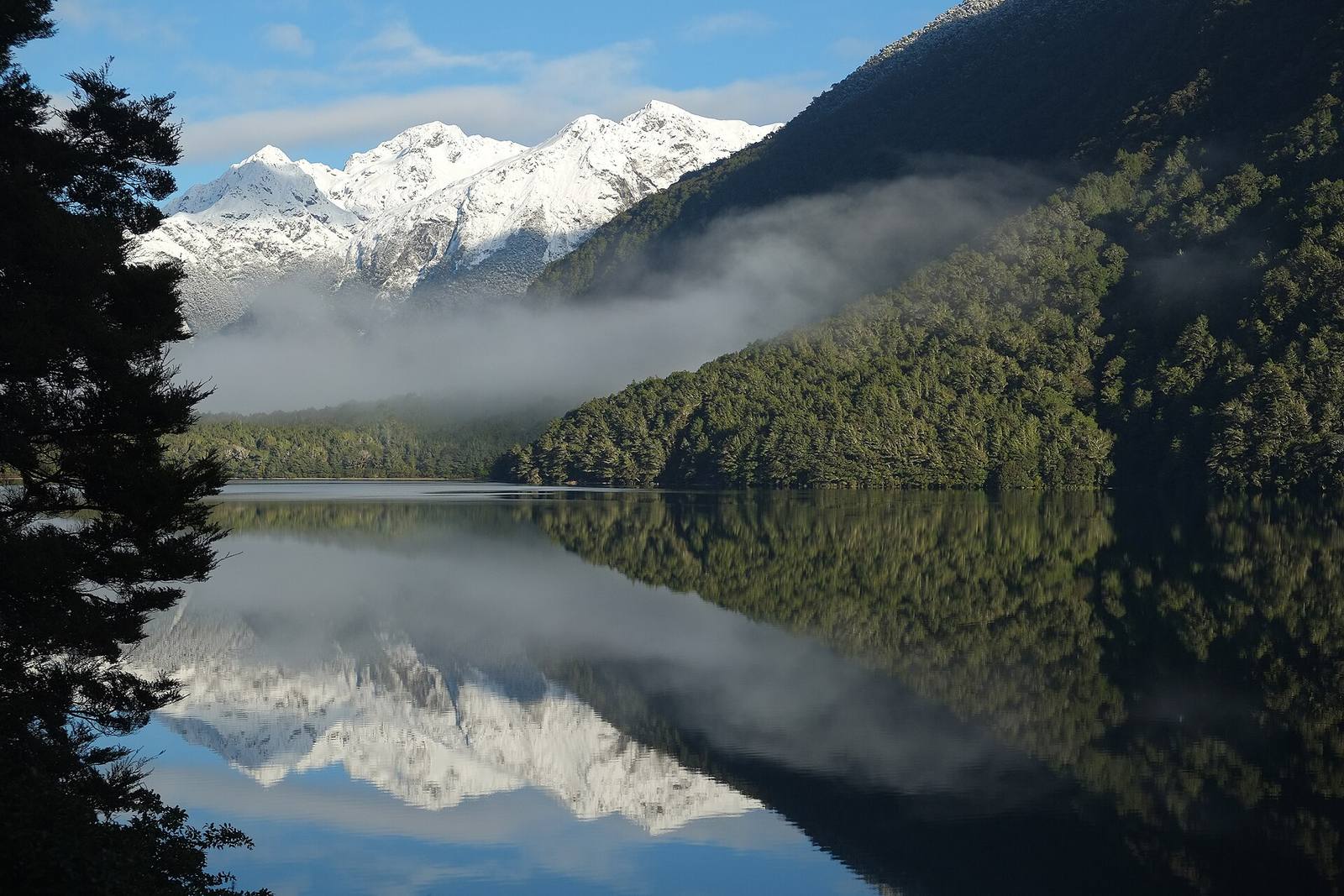 Ruhiger Bergsee, der bei Morgengrauen Schneegipfel spiegelt