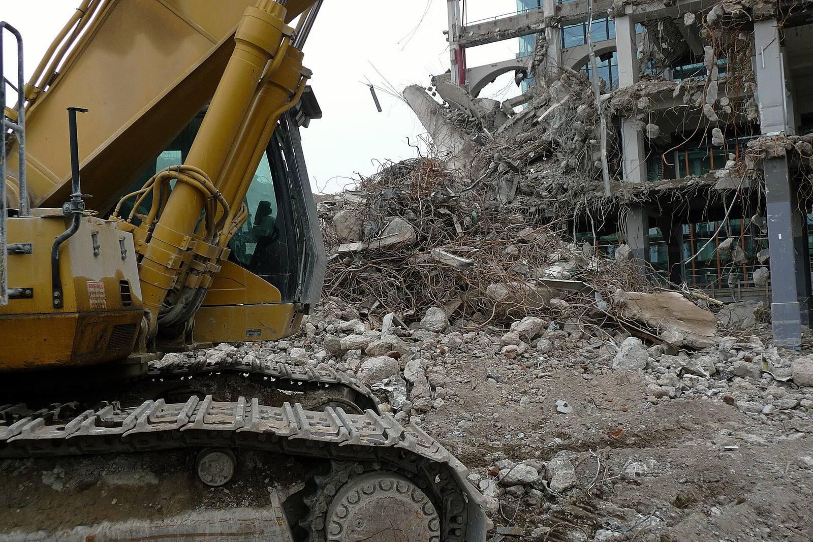 Excavator standing beside a heap of concrete rubble at a demolition site