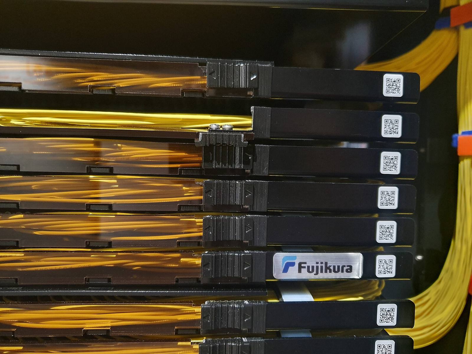 Yellow fibre-optic cables coiled into the trays of a black patch panel