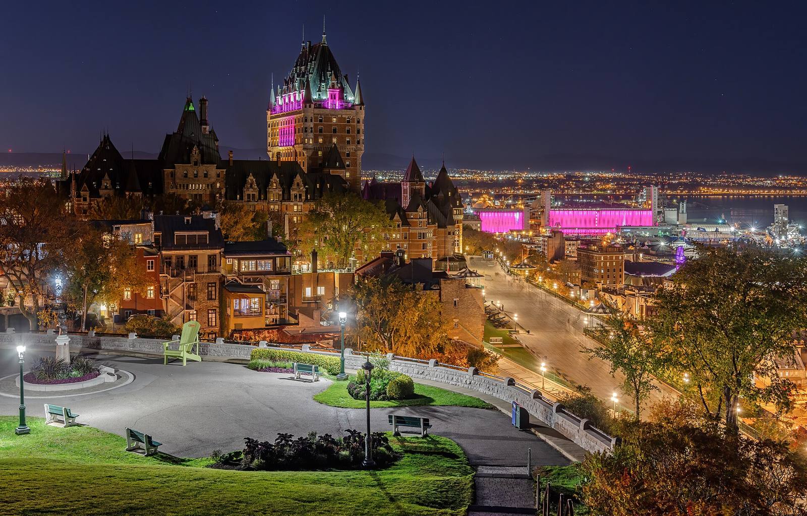 Historic city skyline lit up at night above an illuminated riverside promenade