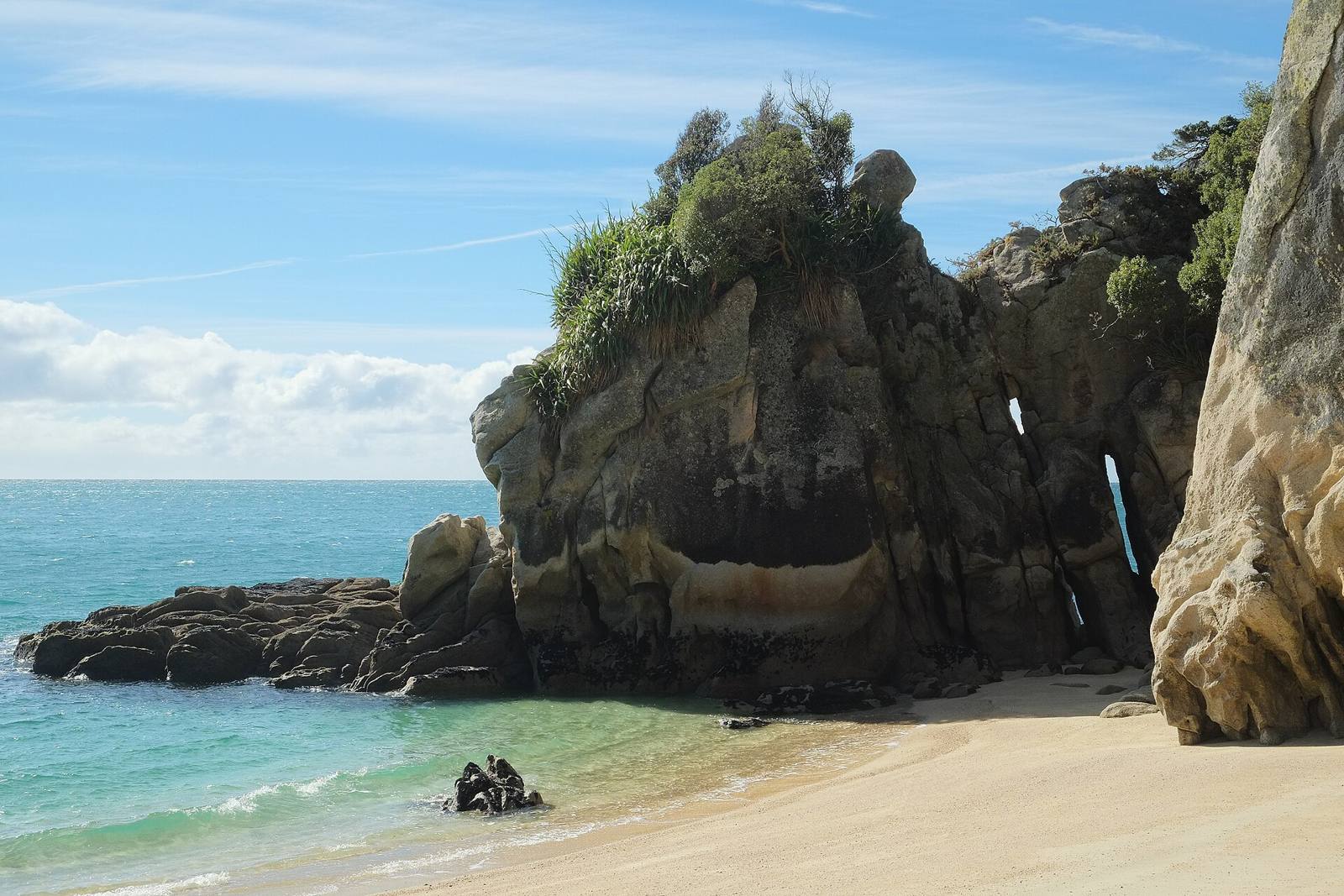 Weathered rock outcrop on a sandy beach beside turquoise sea