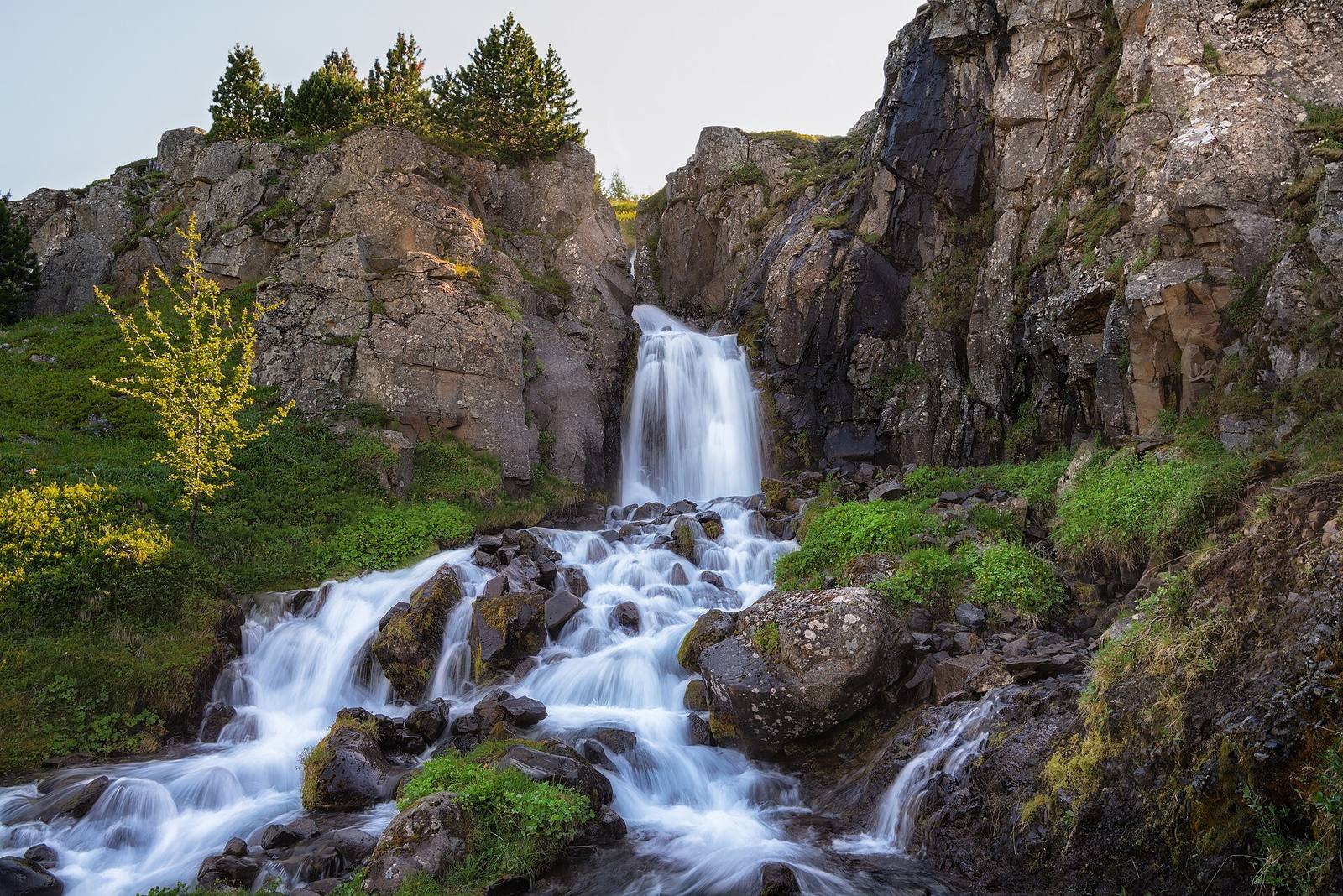 Waterfall cascading over mossy rocks between grassy cliffs